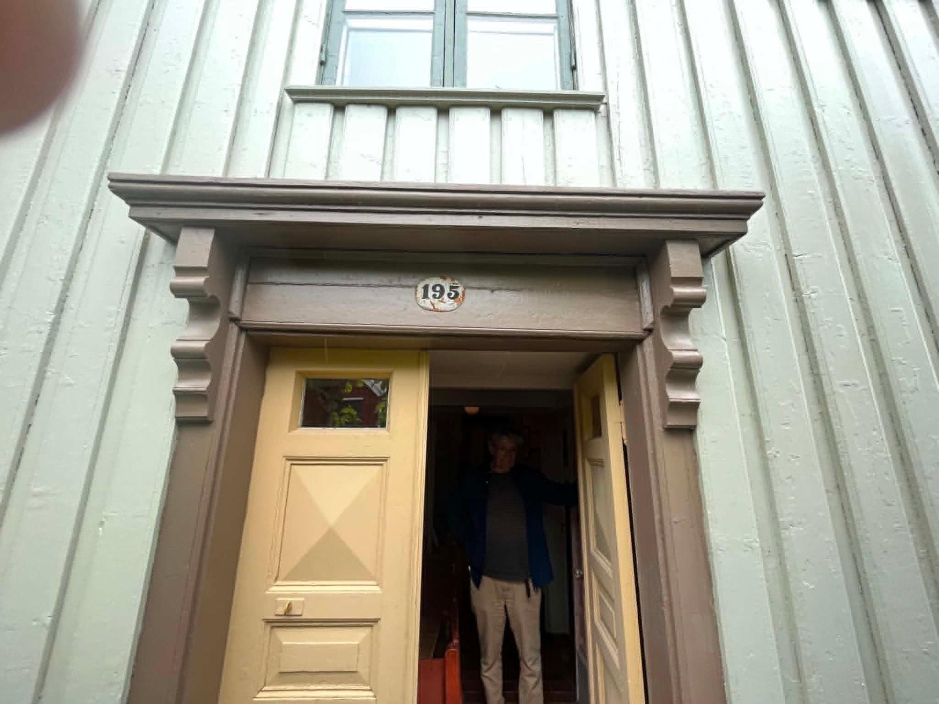 Gammel inngangsdør med profilert dørgerikt og konsoller på hvitmalt trehus